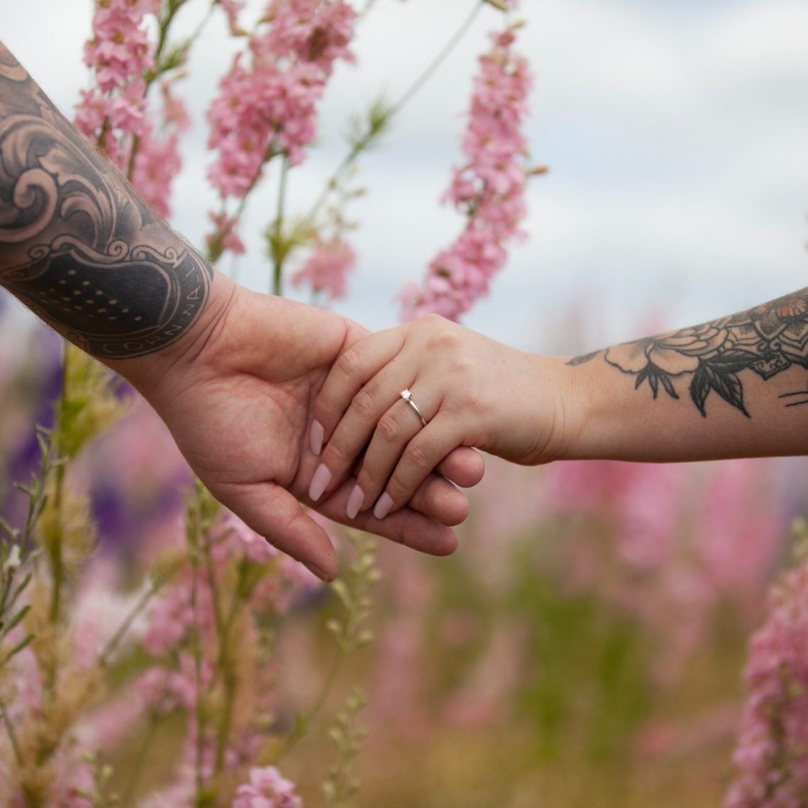 Engagement holding hands Two hands with tattoos holding each other among pink flowers.